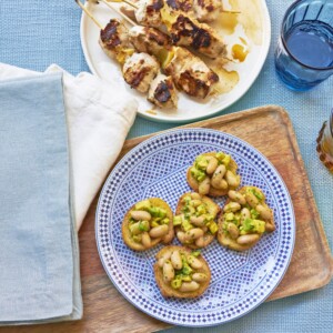 Plate of Avocado And Cannellini Bean Crostini With Gremolata next to a plate of kebabs.
