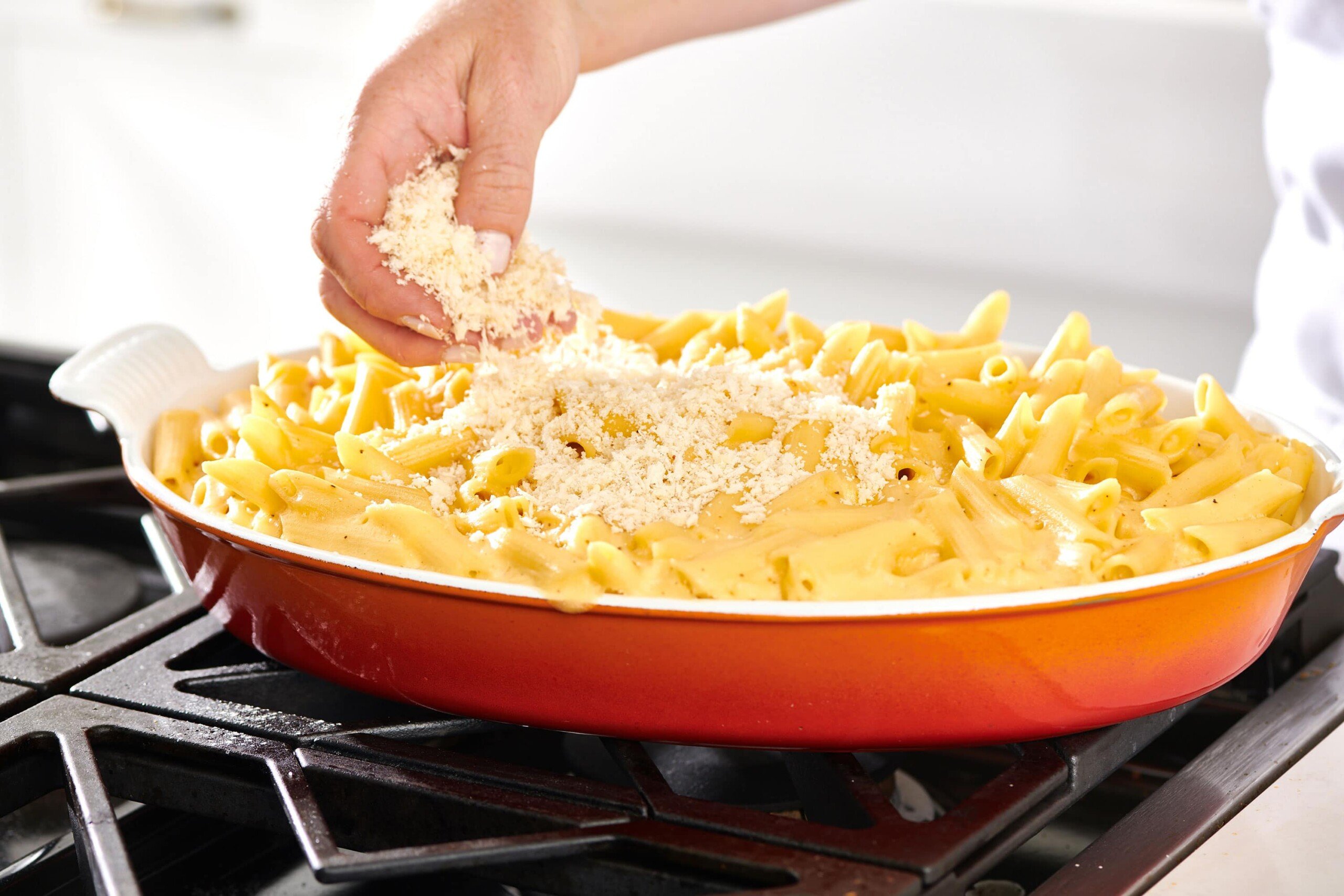 Woman sprinkling panko topping onto a baking pan of macaroni and cheese.