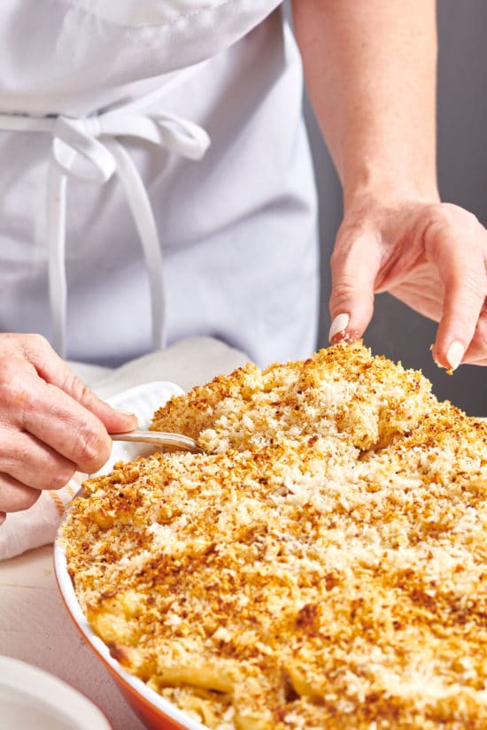 Woman scooping Baked Macaroni and Cheese from a baking dish.