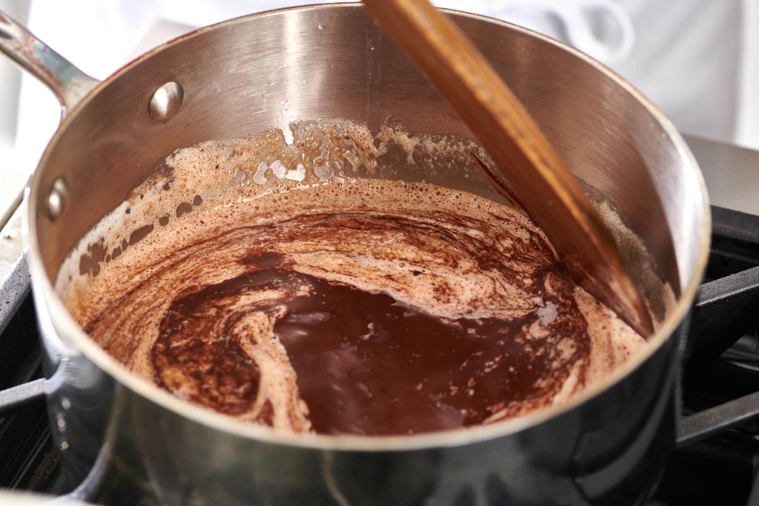 Spoon stirring melted chocolate and butter in saucepan for brownies.