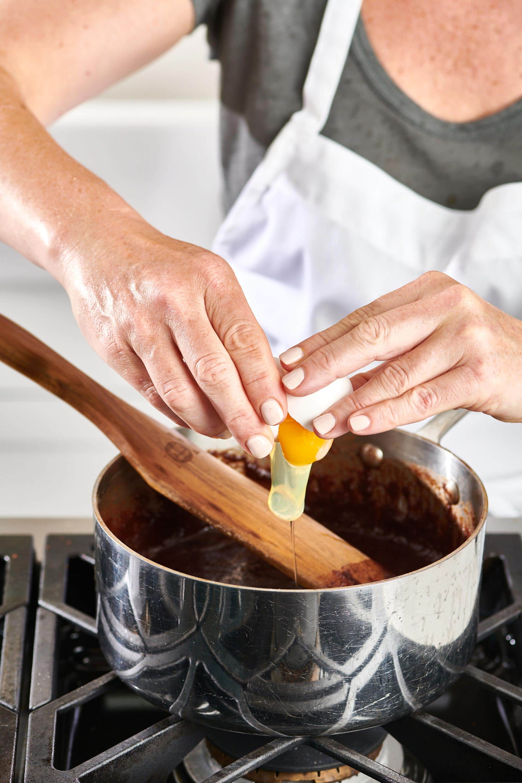 Woman cracking an egg into a pan of chocolate.