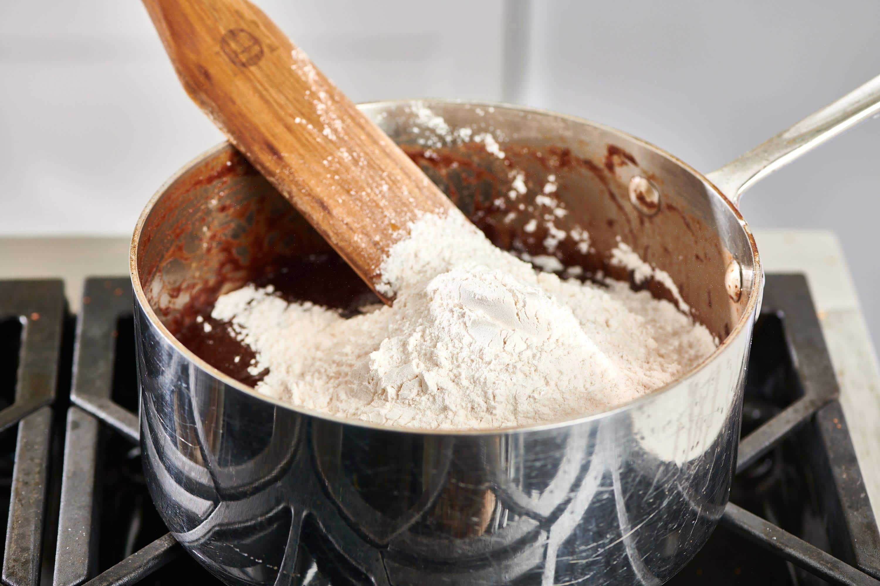 Wooden spatula blending flour into a pot of chocolate.
