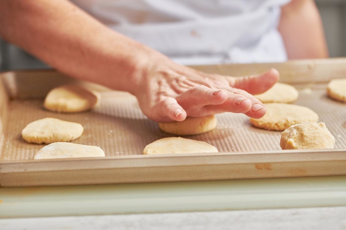 Woman flattening balls of Sugar Cookie dough onto a lined baking sheet.