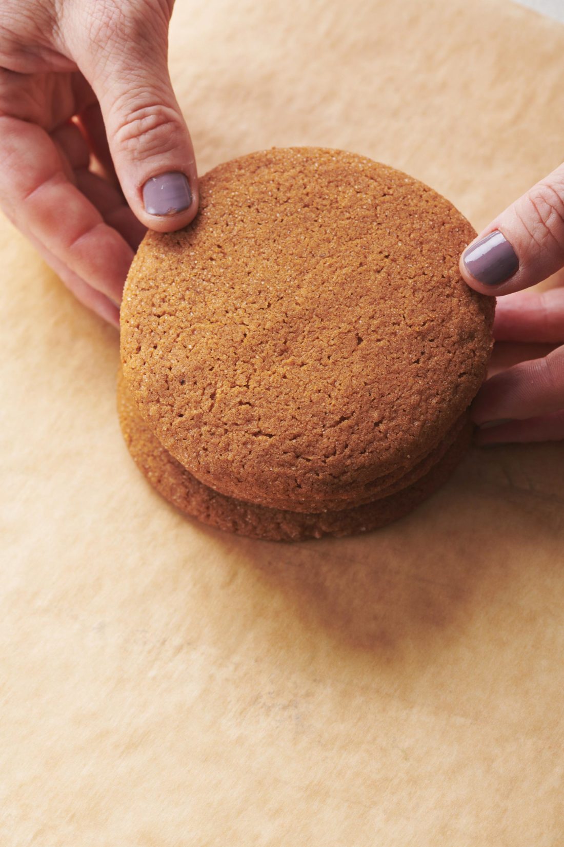 Woman stacking Gingersnaps on parchment paper.