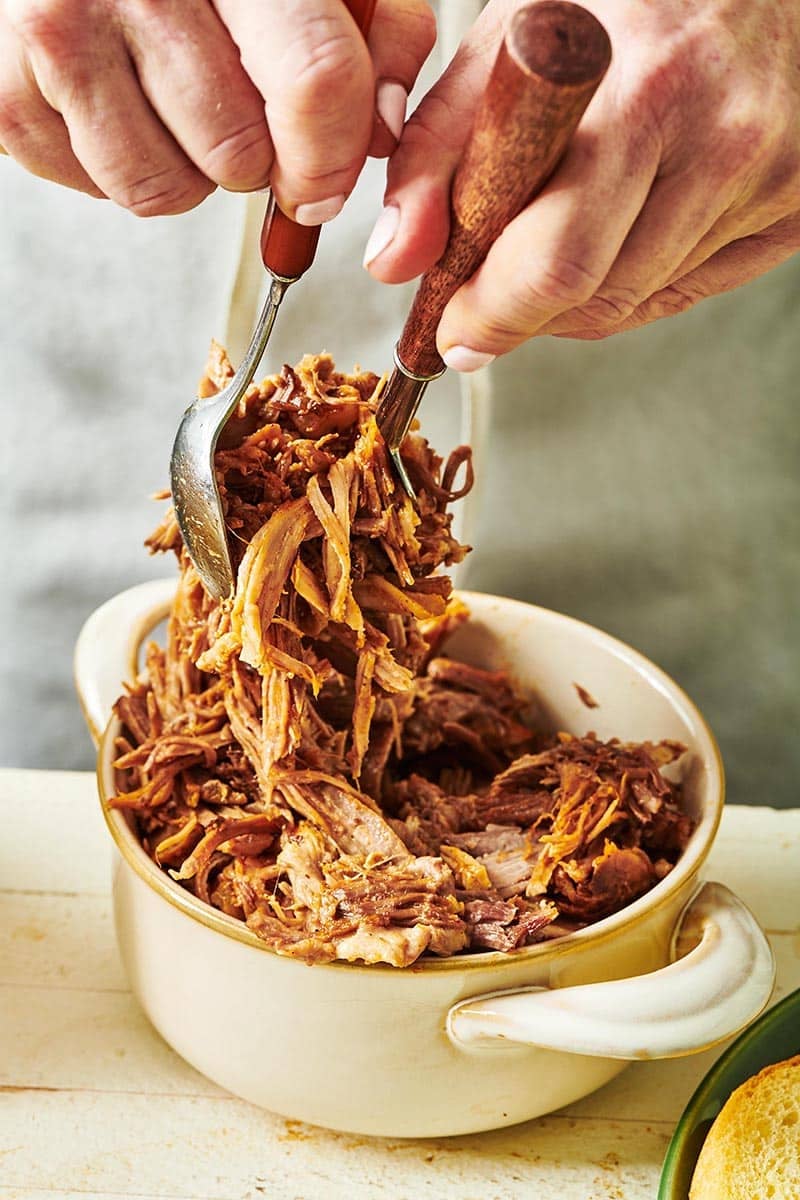 Two spoons grabbing pulled pork from a dish.