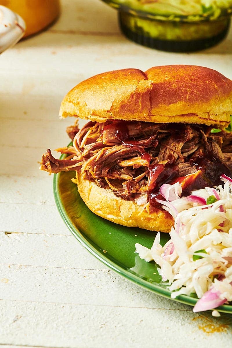 Pulled pork sandwich and coleslaw on green plate.