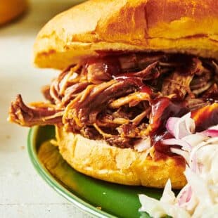 BBQ pulled pork sandwich with cole slaw on green plate.