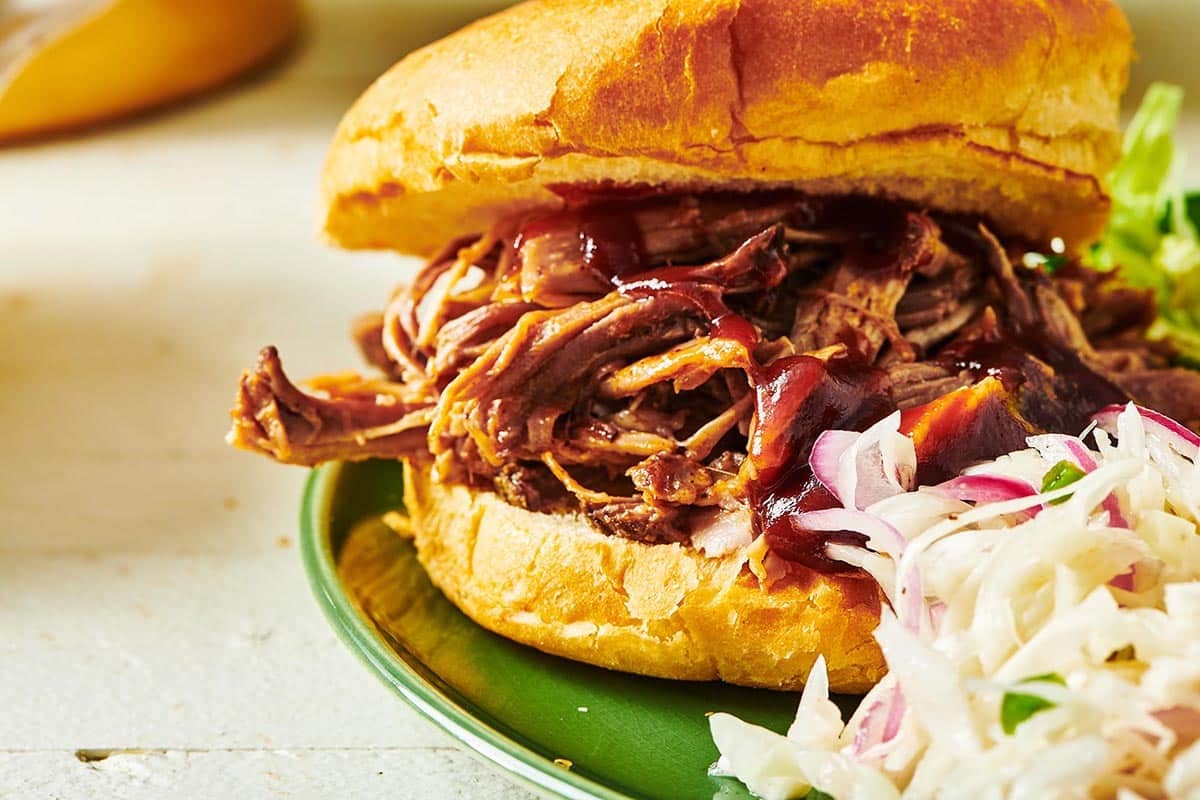 BBQ pulled pork sandwich with cole slaw on green plate.