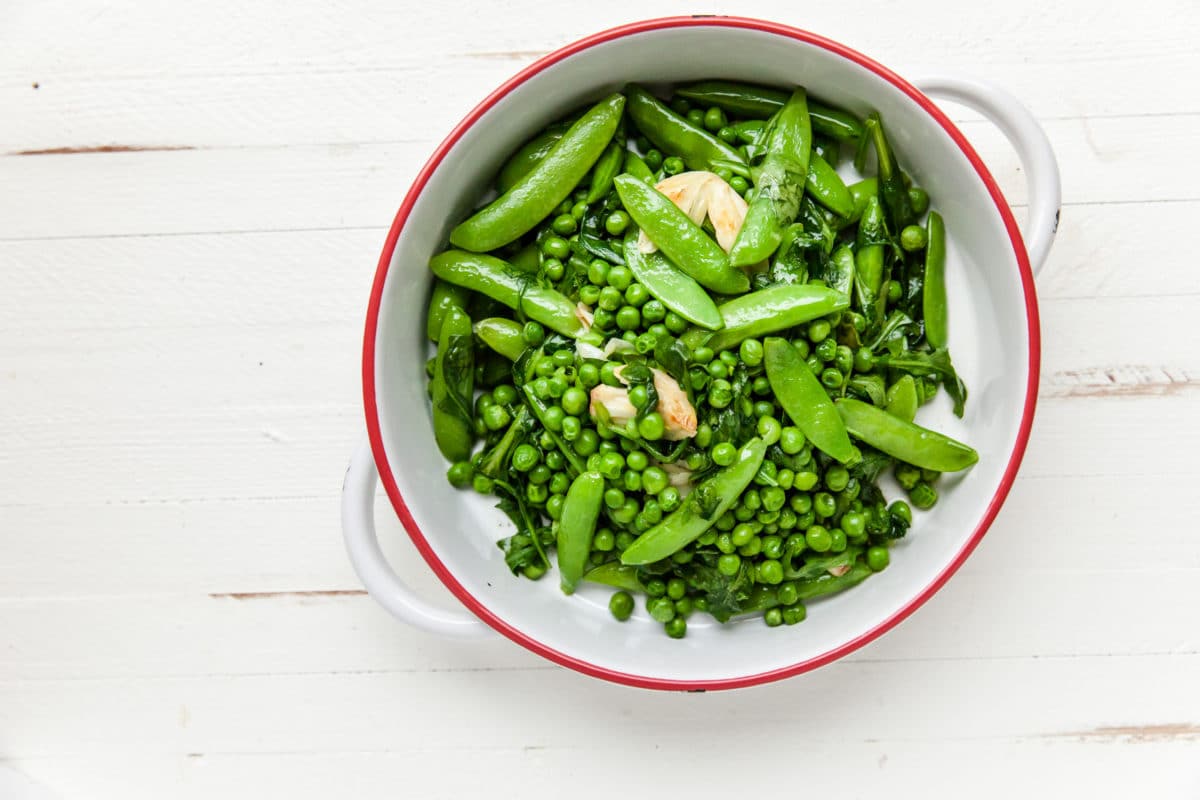 Green peas, sugar snap peas, garlic, arugula, and spinach in white bowl.