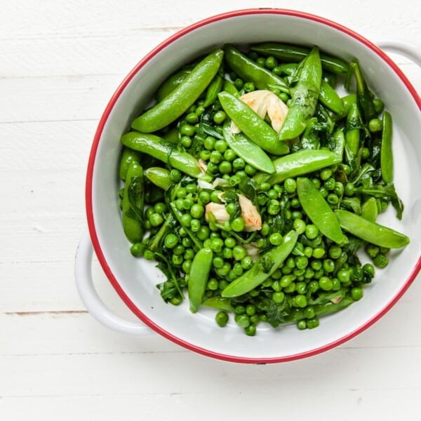 Green peas, sugar snap peas, garlic, arugula, and spinach in white bowl.