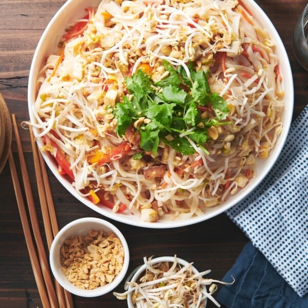 Large, white serving bowl of Pad Thai on a wooden table.