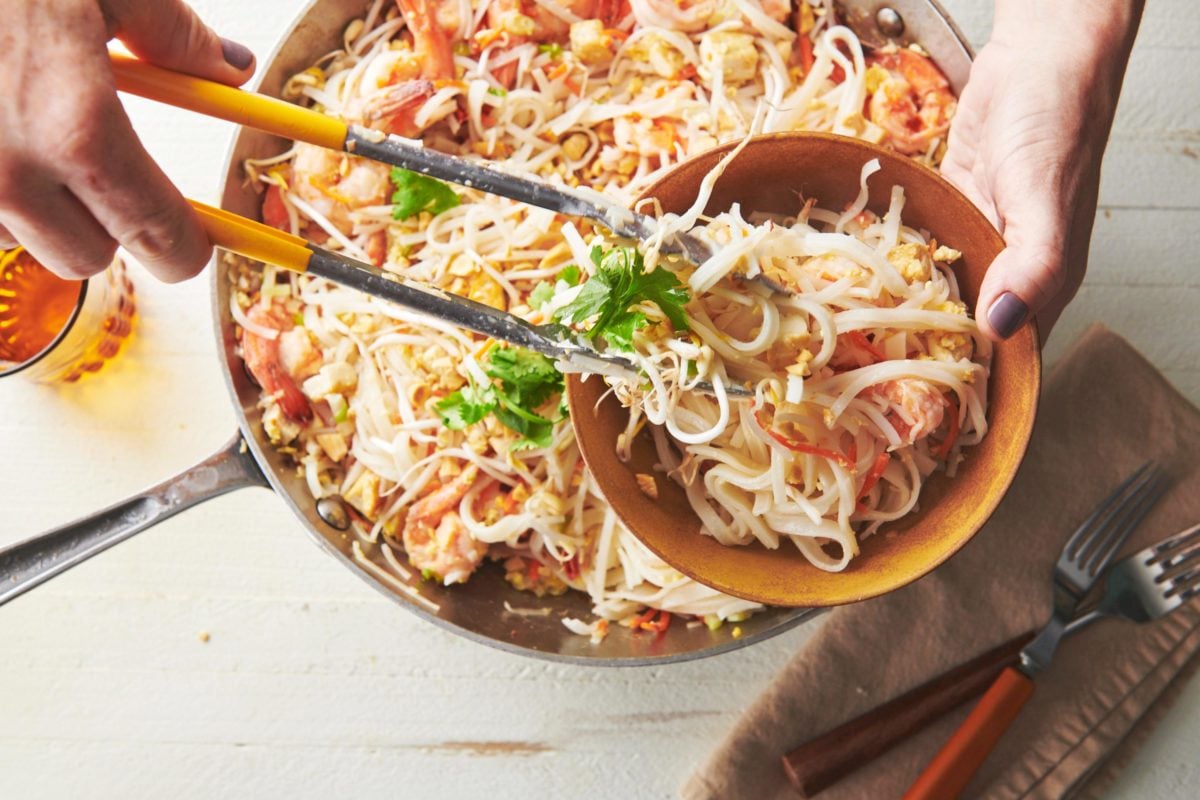 Tongs serving Pad Thai into a bowl.