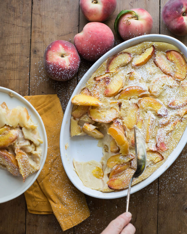 Spoon scooping Peach Clafoutis onto a plate.