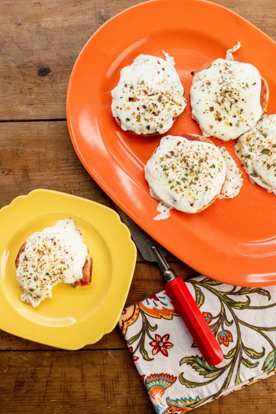English Muffin Pizzas on a yellow plate and an orange platter.