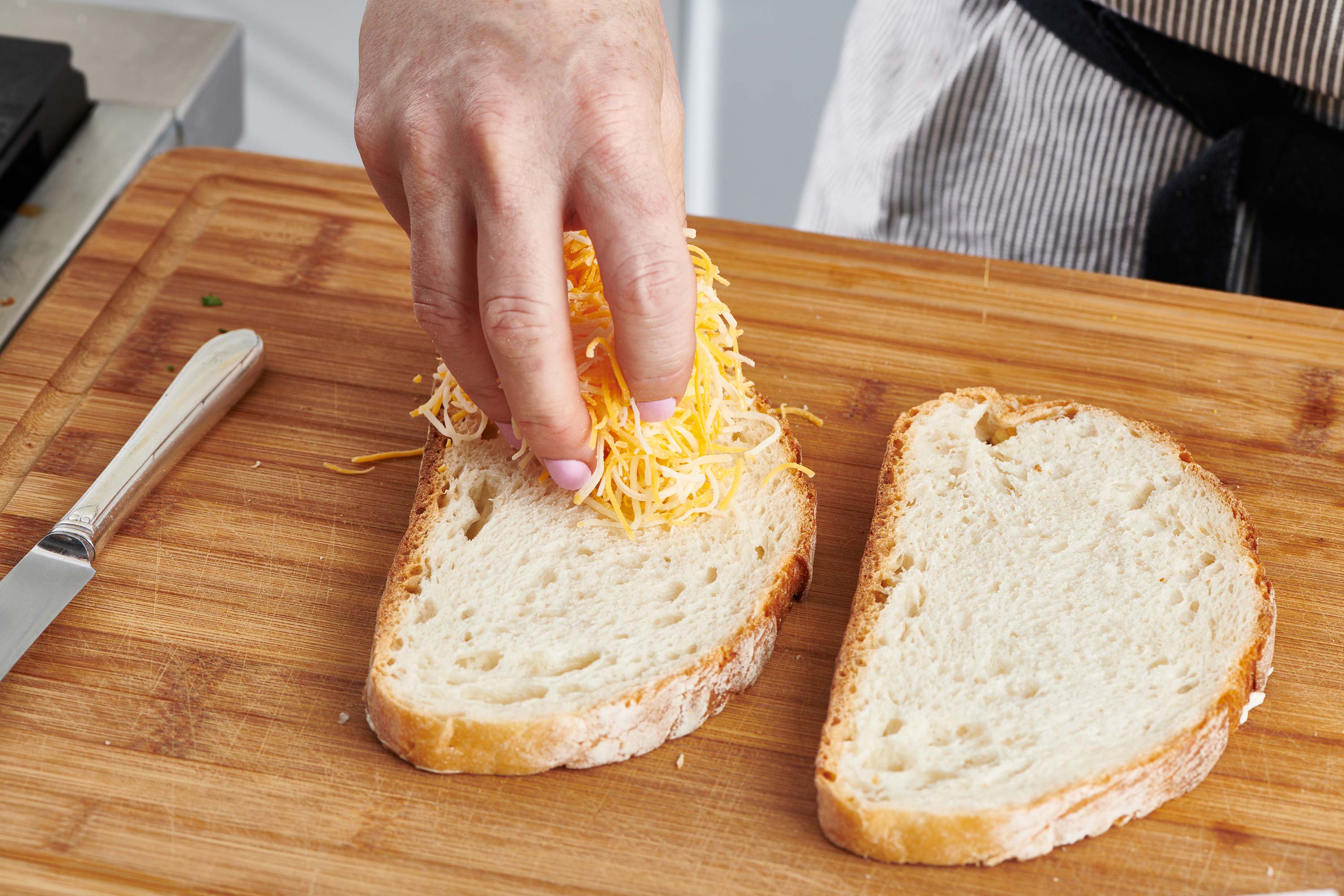Woman topping slice of bread with shredded cheese.