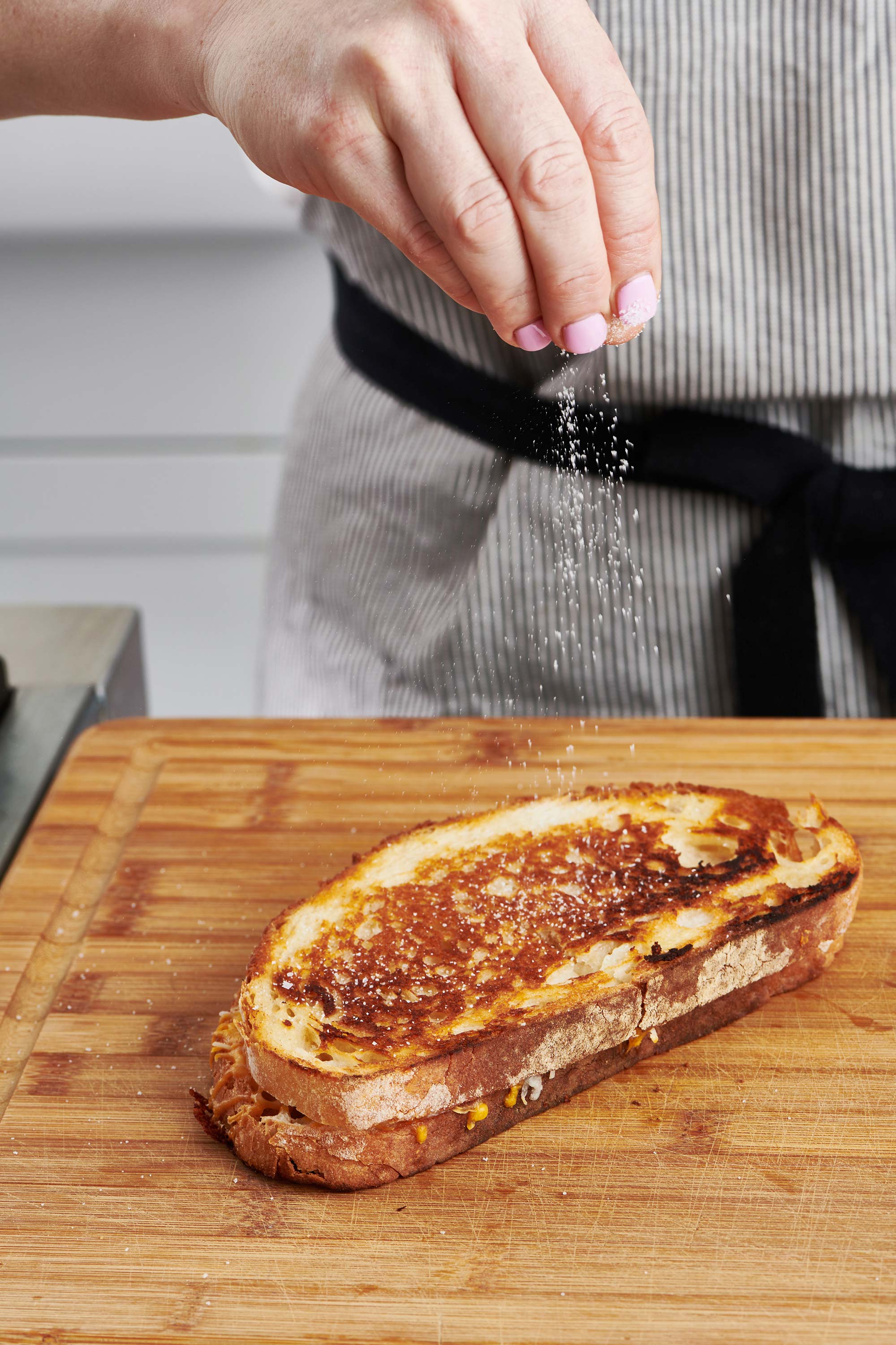 Woman sprinkling salt onto a toasted grilled cheese sandwich.