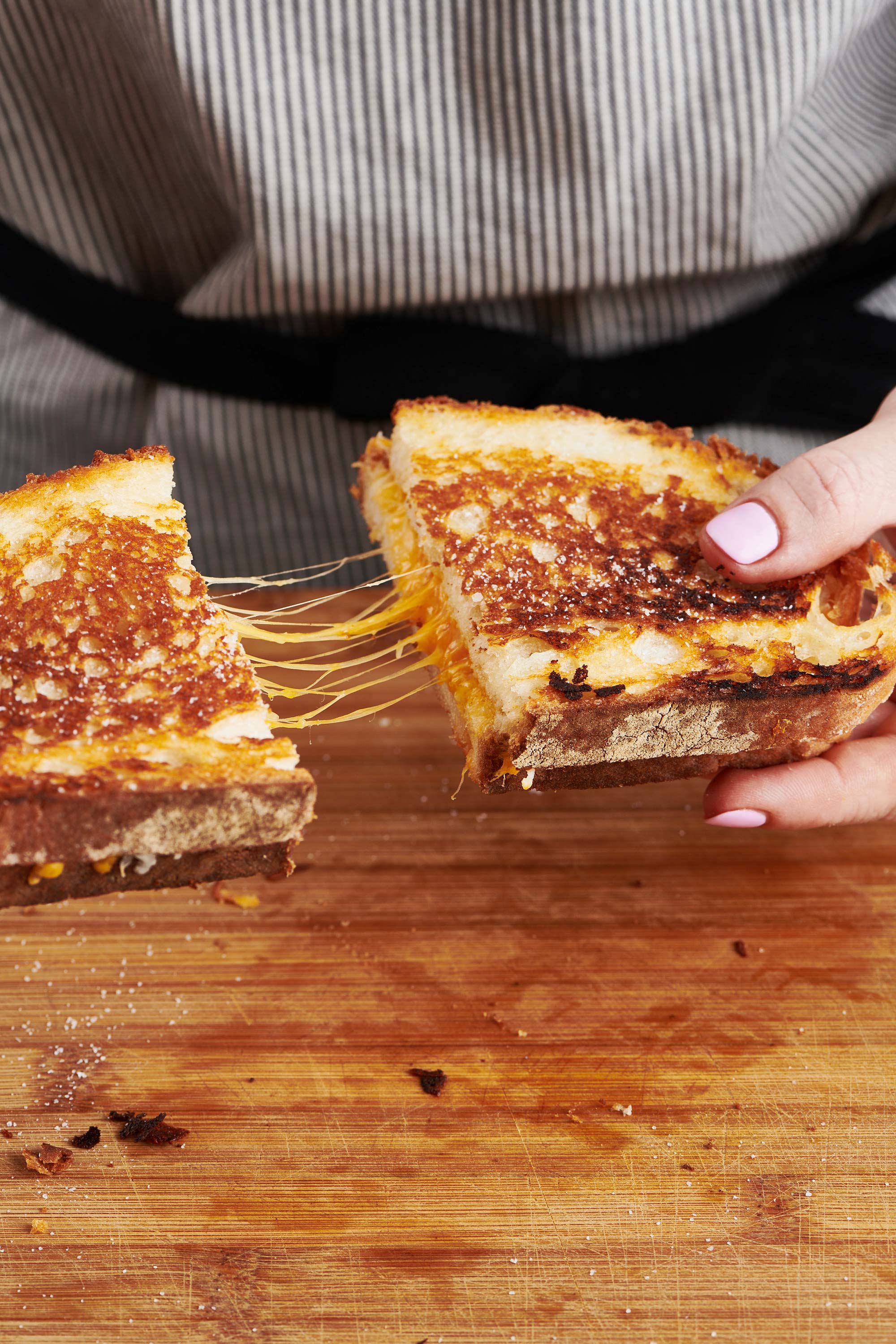 Woman pulling apart a warm grilled cheese sandwich cut in half.