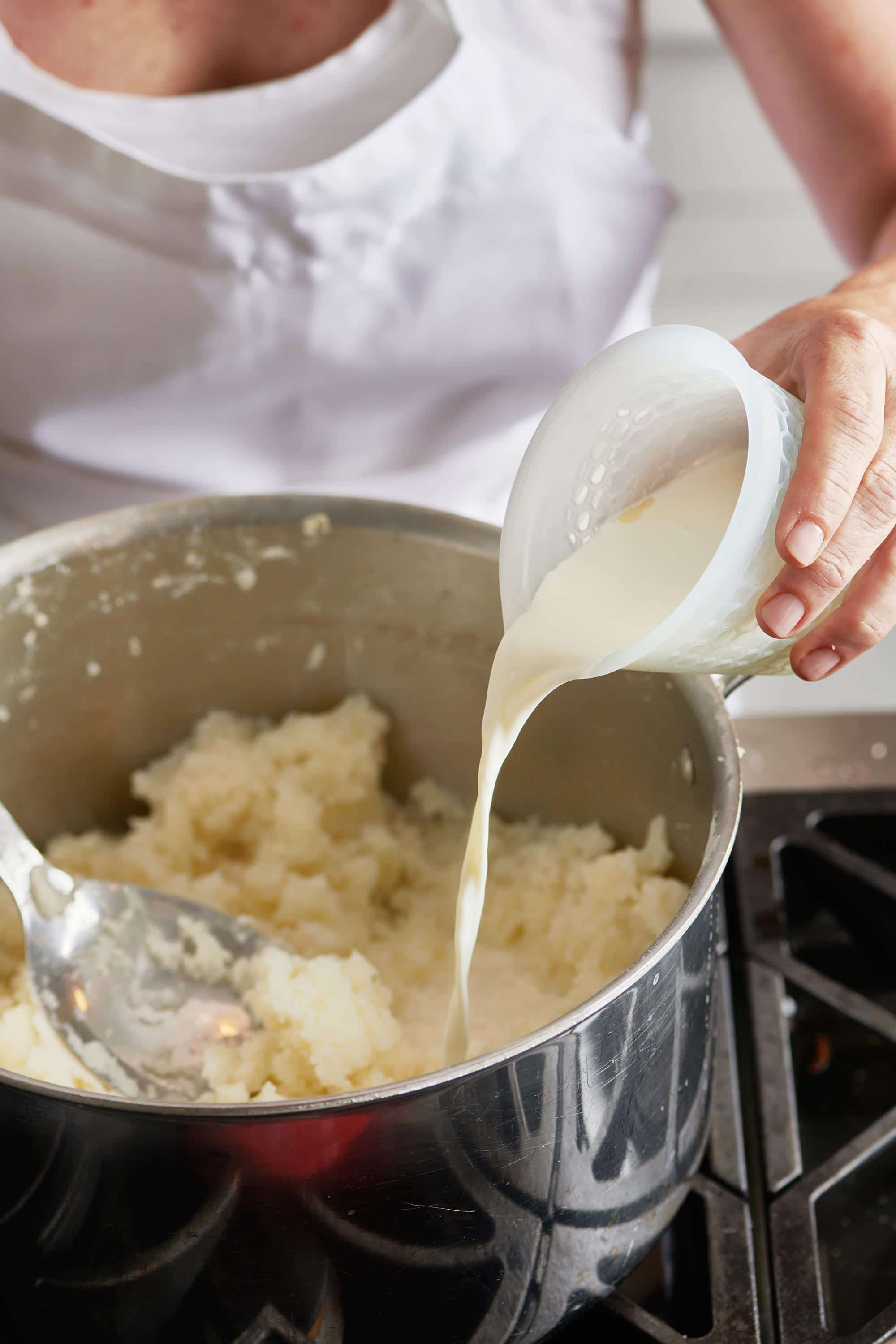 Woman pouring cream into pot of mashed potatoes.