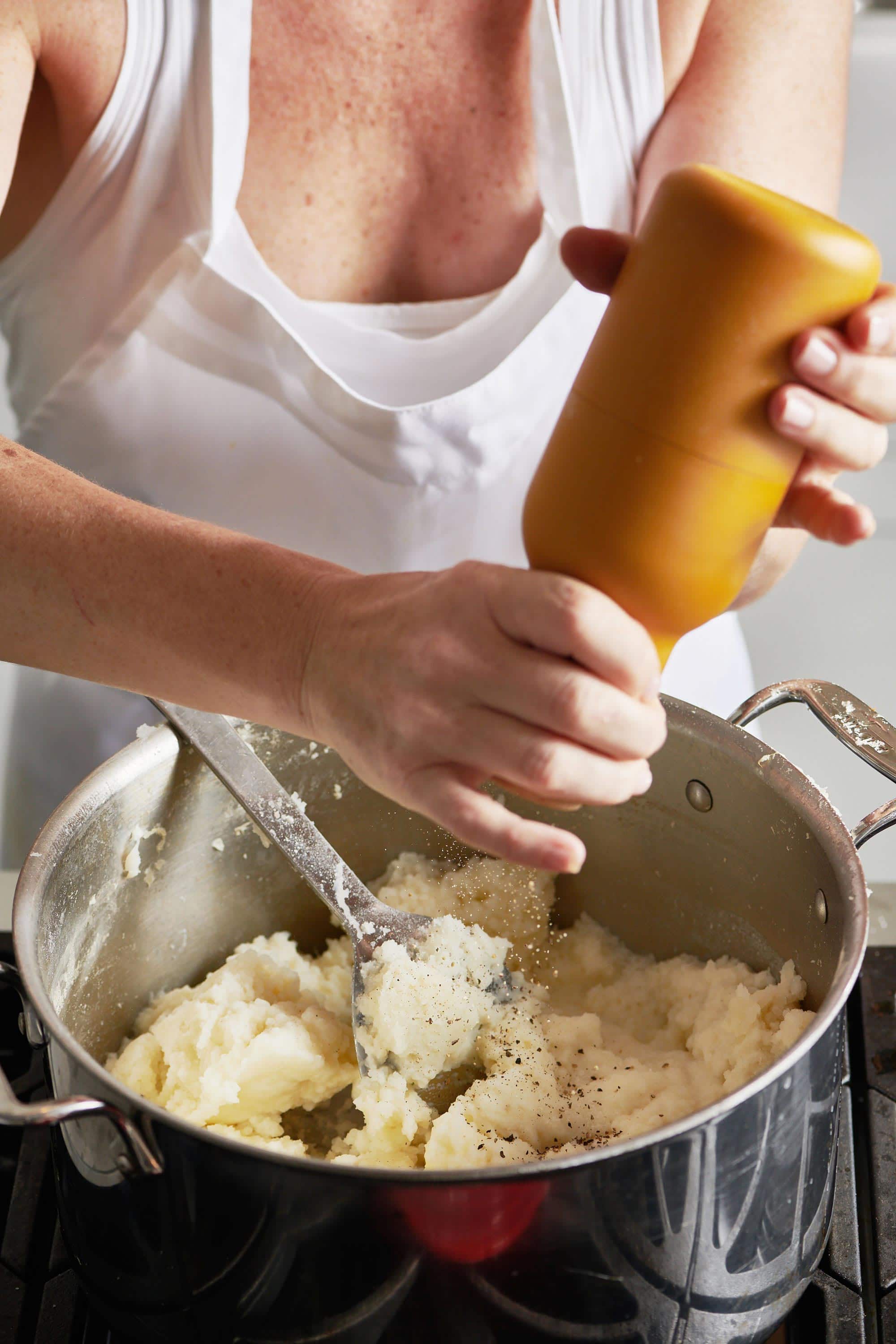 Woman grinding pepper into a pot of mashed potatoes.