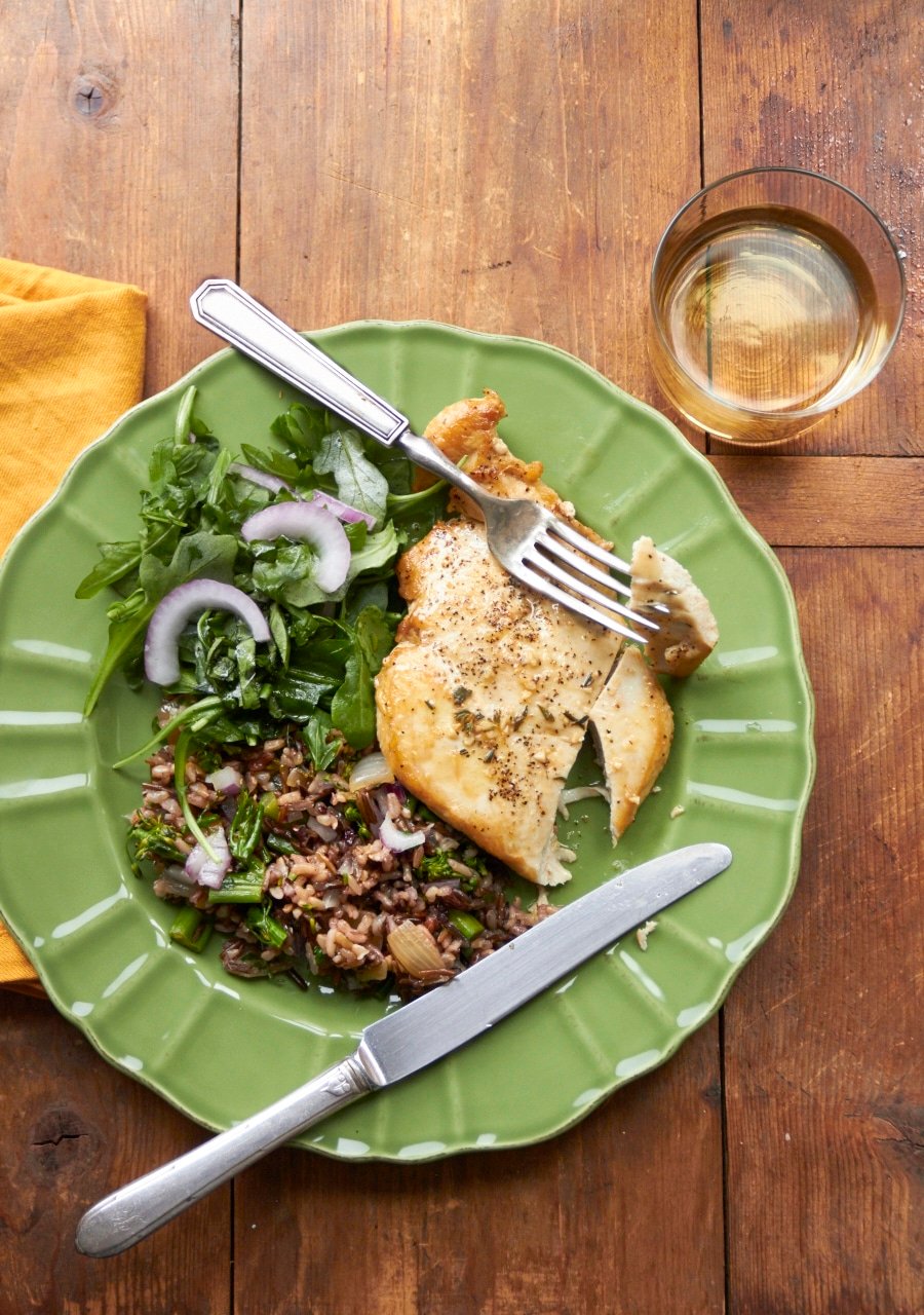 Chicken with pan sauce and wild rice with a salad on a plate.