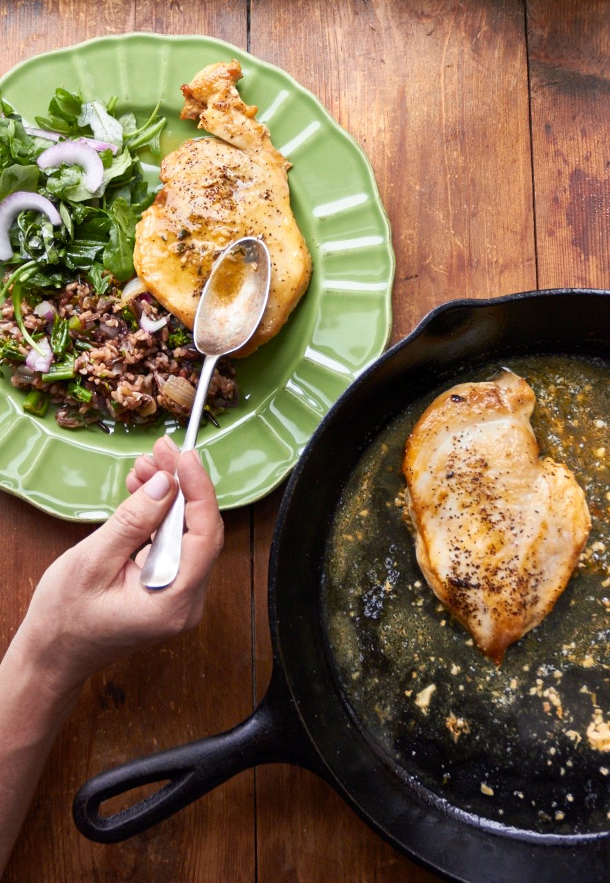 Woman spooning pan sauce over a chicken breast.