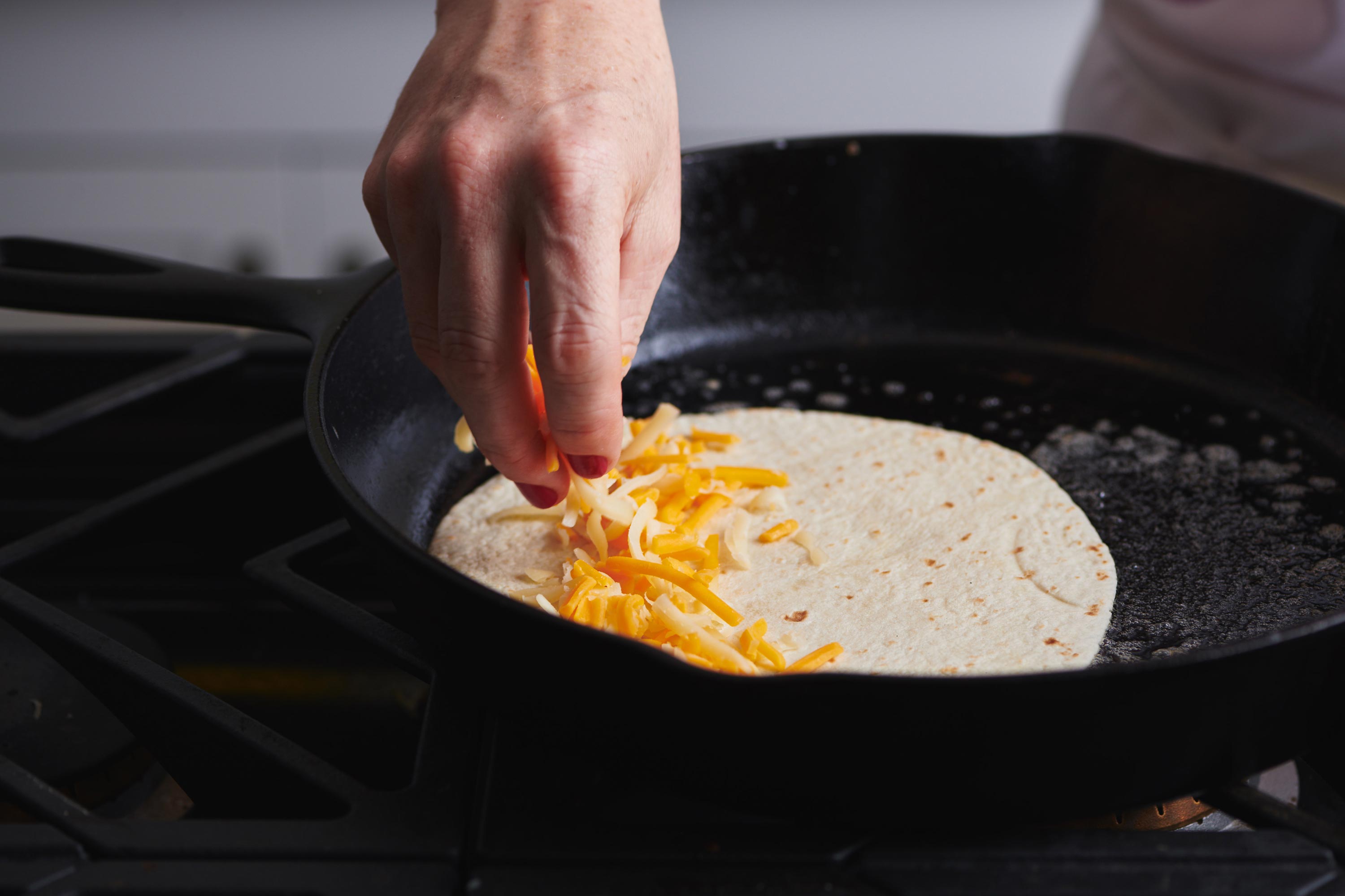 Woman sprinkling cheese on a quesadilla in a cast iron pan.