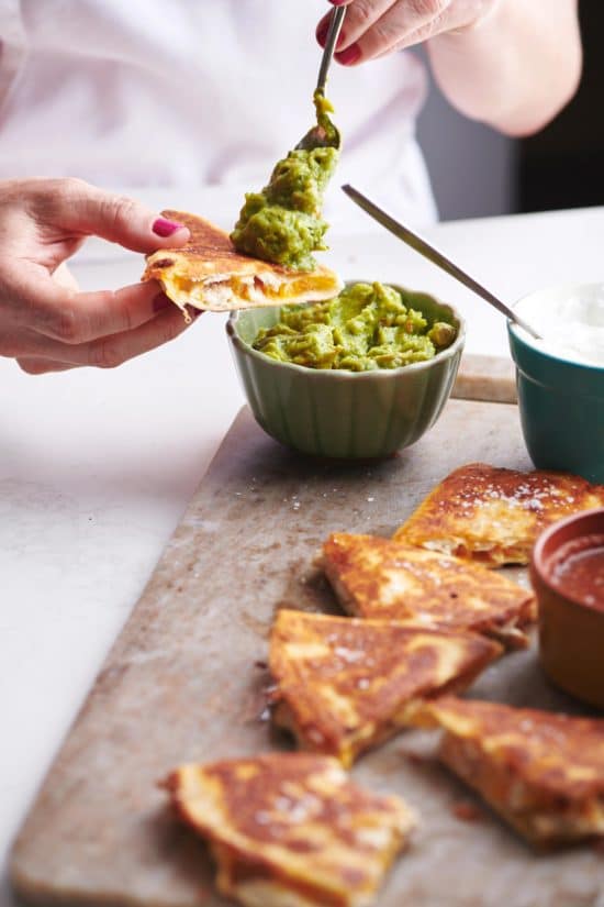 Woman scooping guacamole onto a Rotisserie Chicken and Cheese Quesadilla.