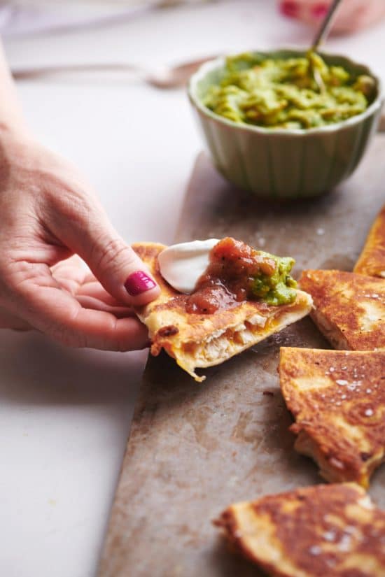 Woman holding a Rotisserie Chicken and Cheese Quesadilla topped with guacamole, salsa, and sour cream.