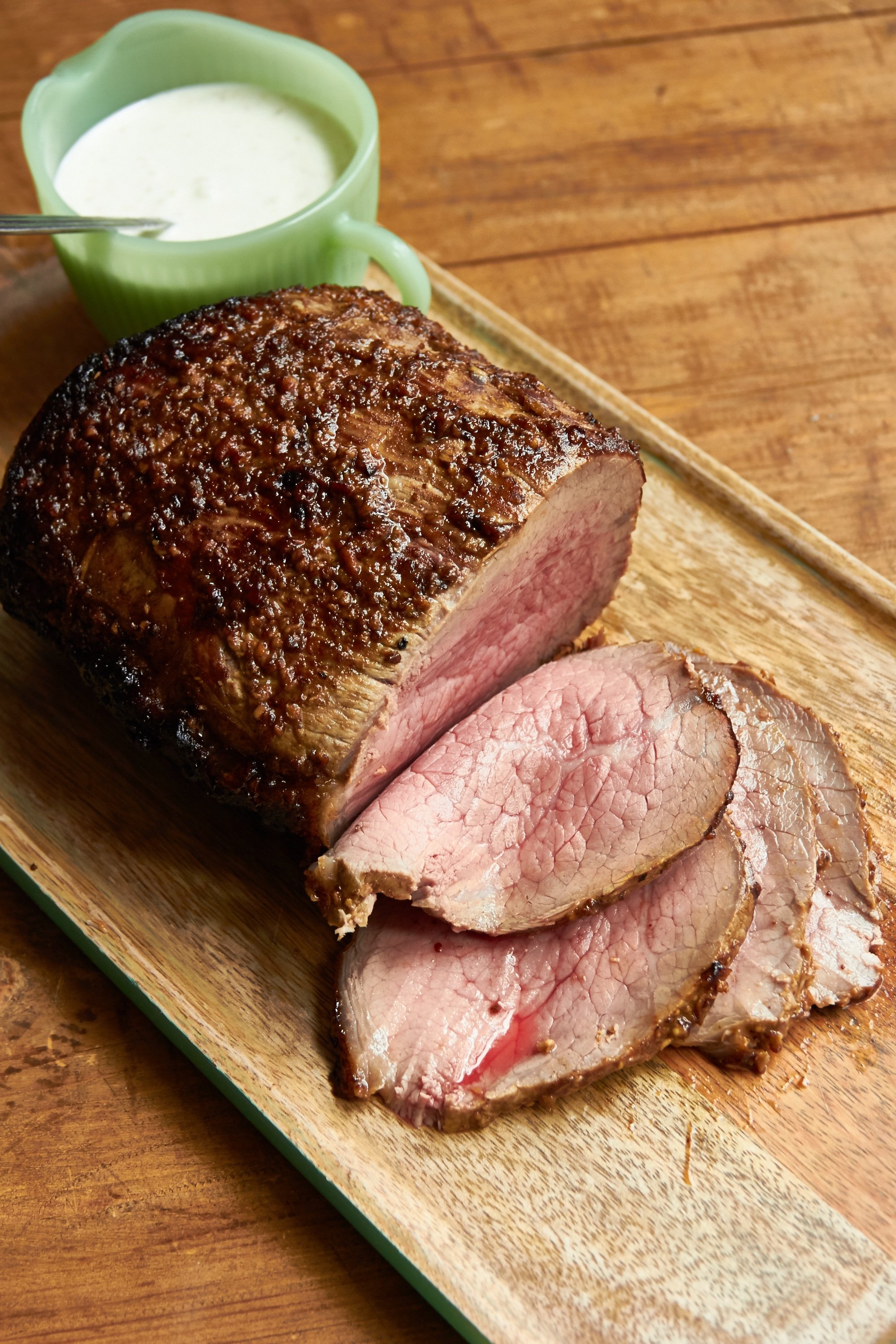 Partially-sliced Roast Beef with Mustard Garlic Crust on a wooden surface.