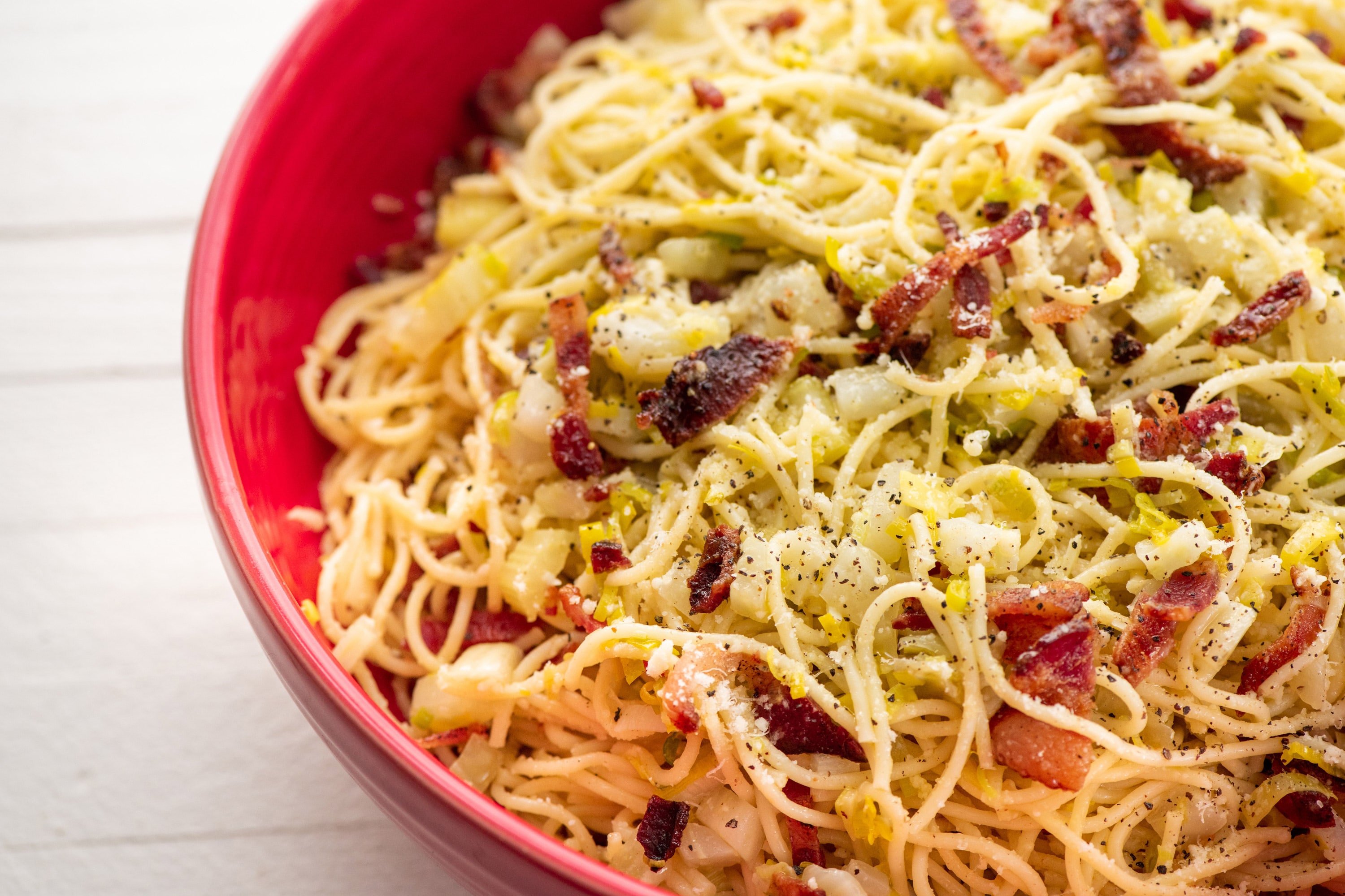 Red bowl with spaghetti, fennel, bacon, and Parmesan cheese.