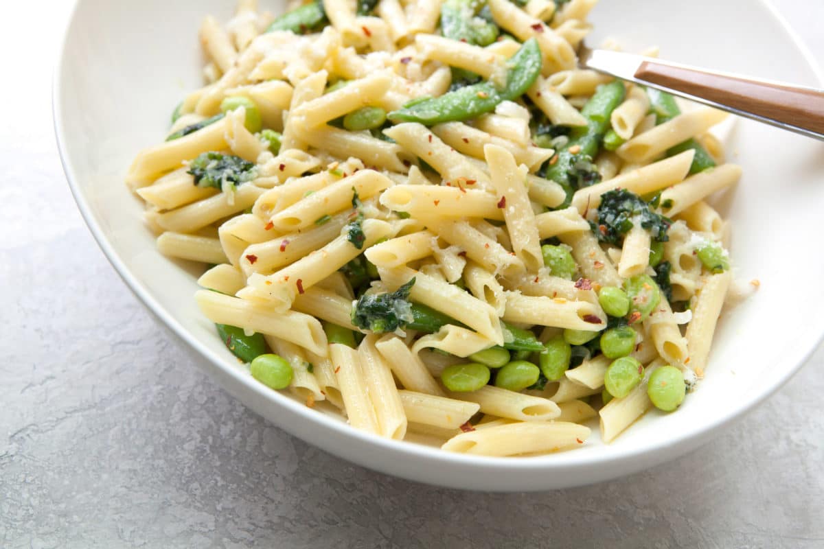 Pasta with Ramps, Edamame, and Sugar Snap Peas in a Light Parmesan Cream Sauce in white bowl.