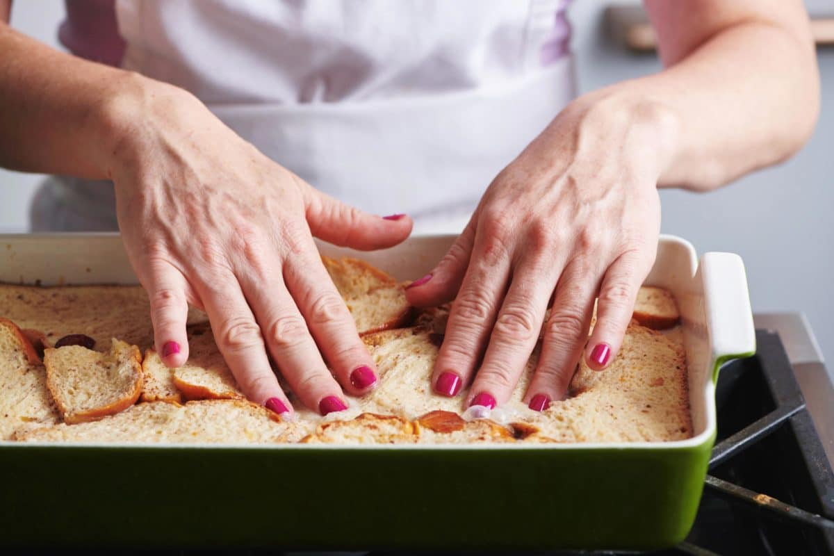 Woman placing bread into a baking dish with egg mixture.