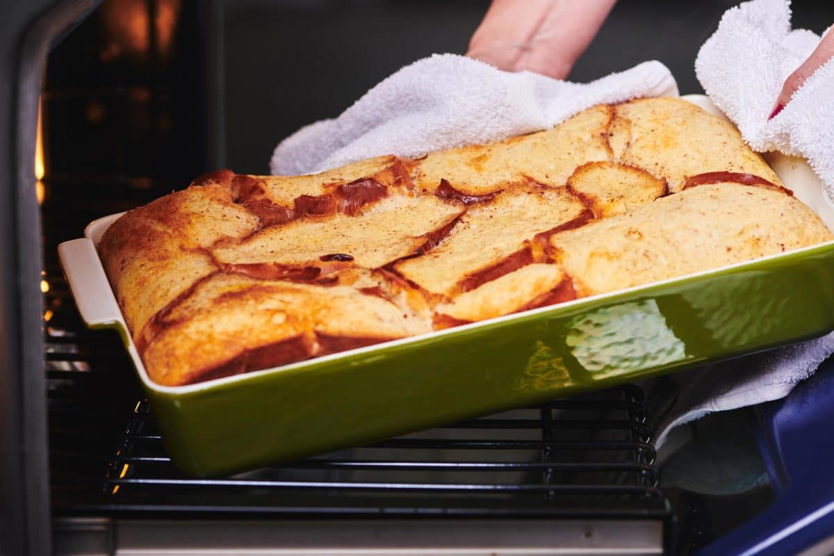 Woman grabbing a green baking dish of  French Toast from the oven.