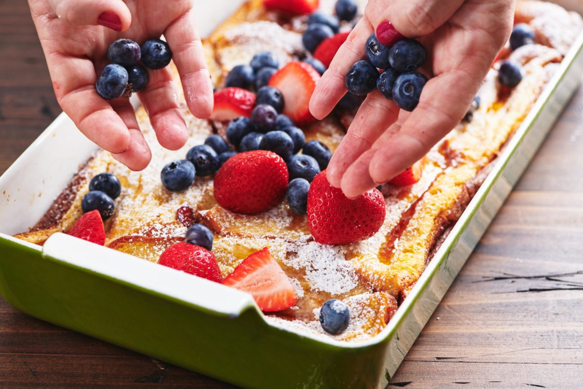 Woman placing berries onto a baking dish of  French Toast.
