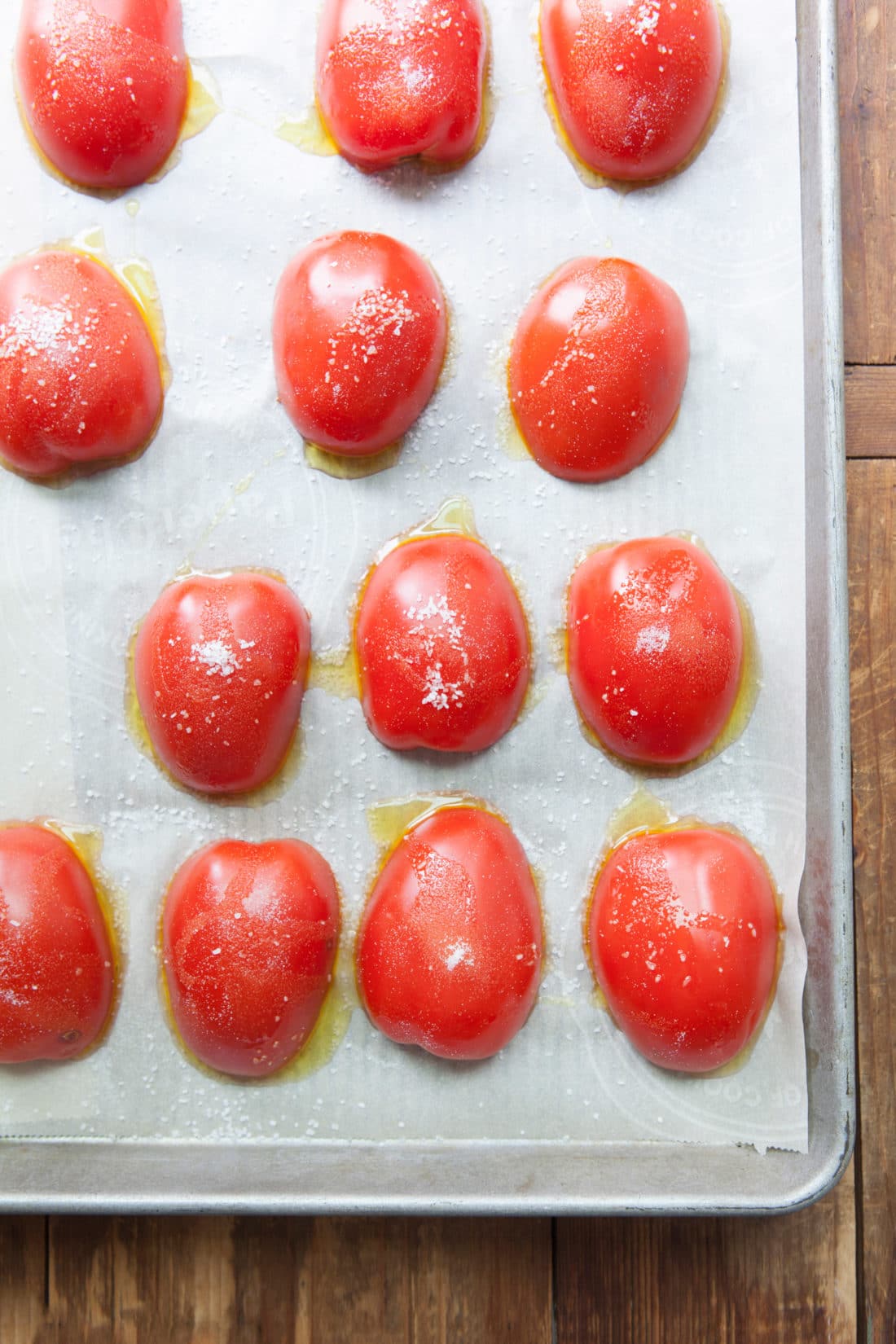 Lined baking sheet topped with halved tomatoes seasoned with olive oil and salt.