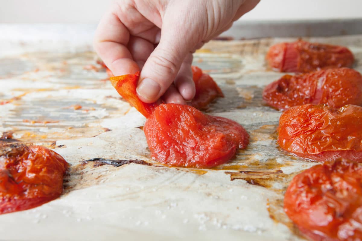 Person removing the skin from a roasted tomato.