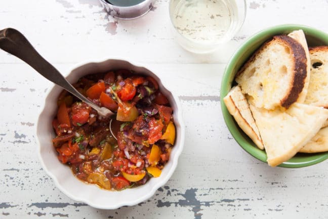 Bowl of Herbed Roasted and Raw Tomato Salsa with Olives on a table with bread.