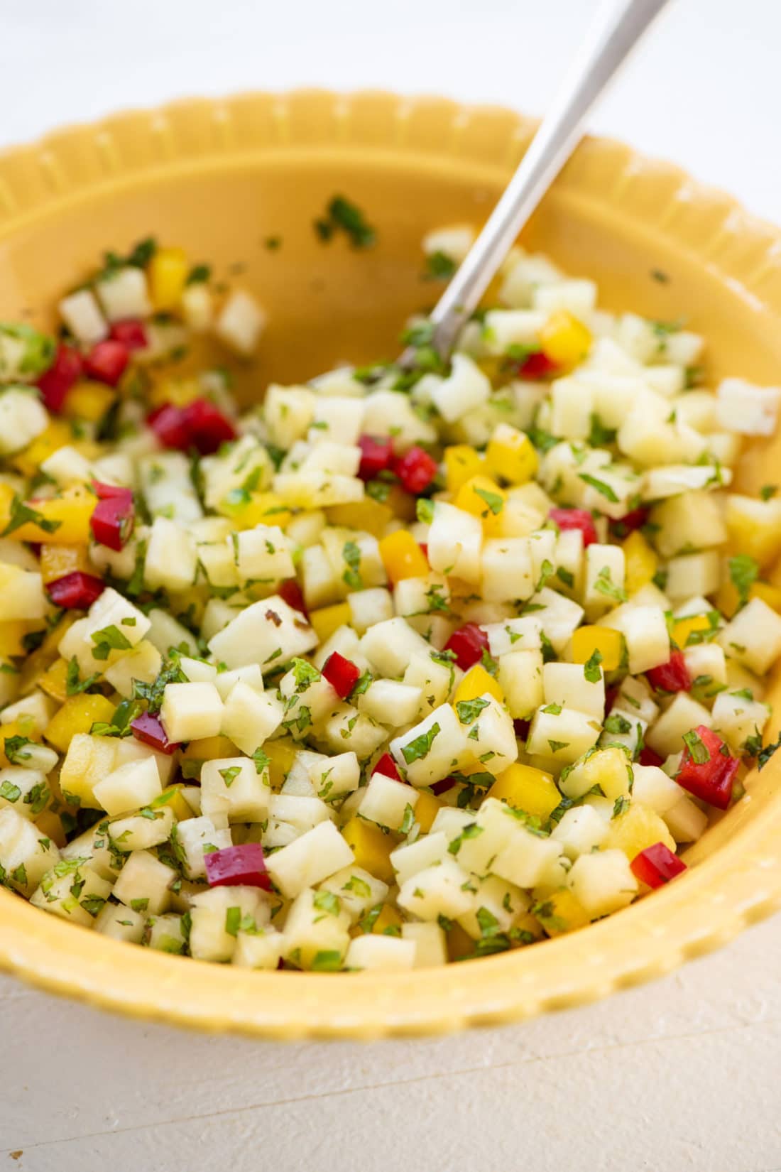 Spoon in a yellow bowl of Pineapple Mint Jalapeno Salsa.