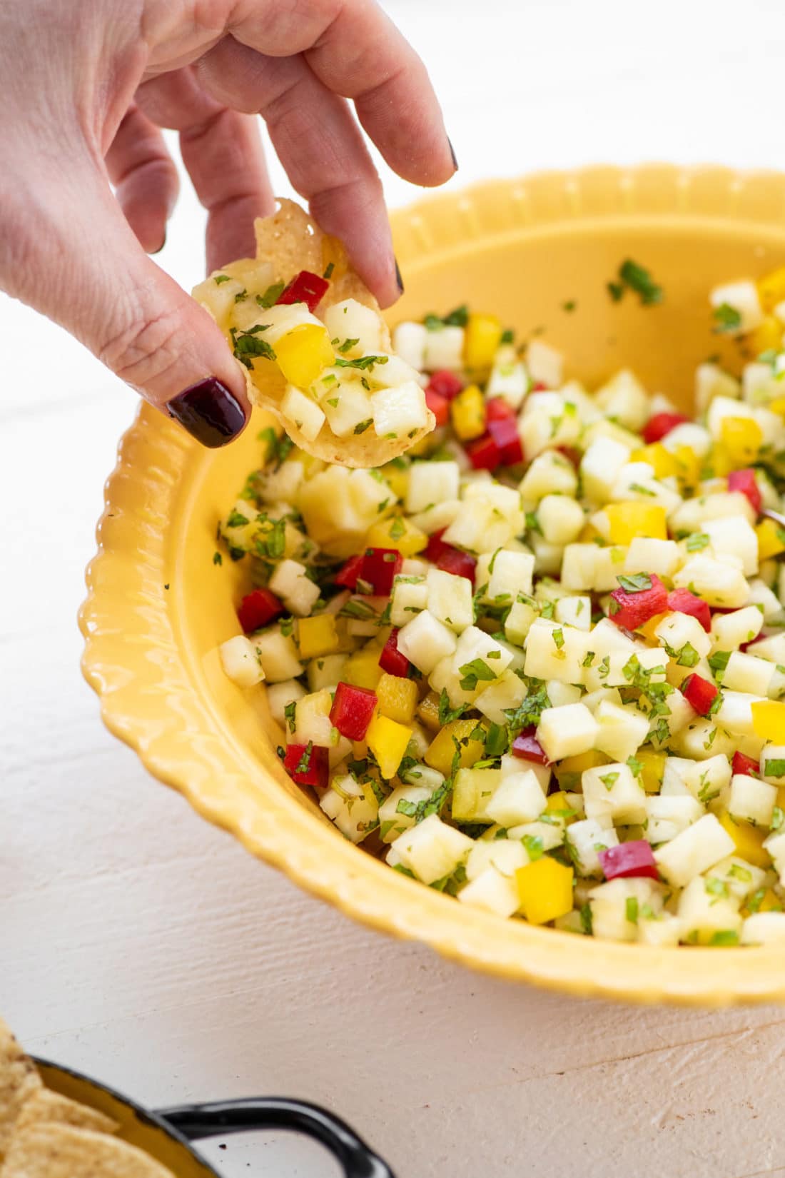 Woman scooping a chip into a bowl of Pineapple Mint Jalapeno Salsa.