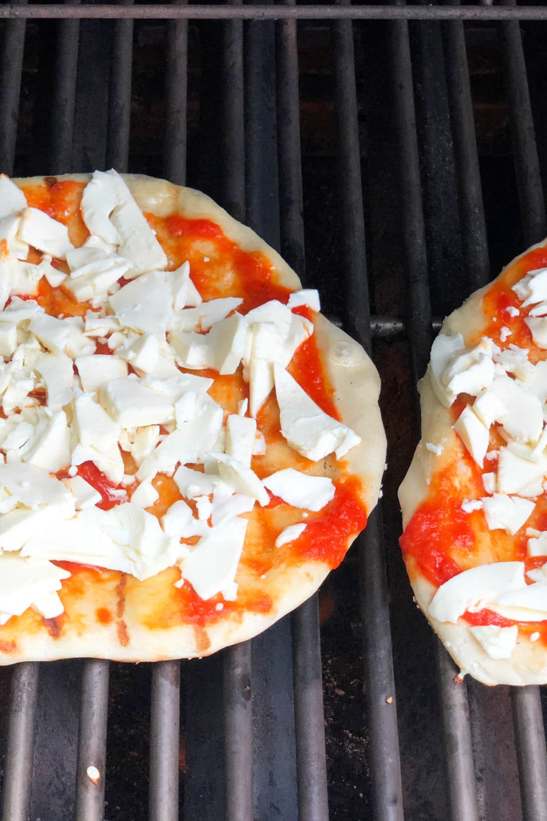 Two pizzas with sauce and cheese on the grill.