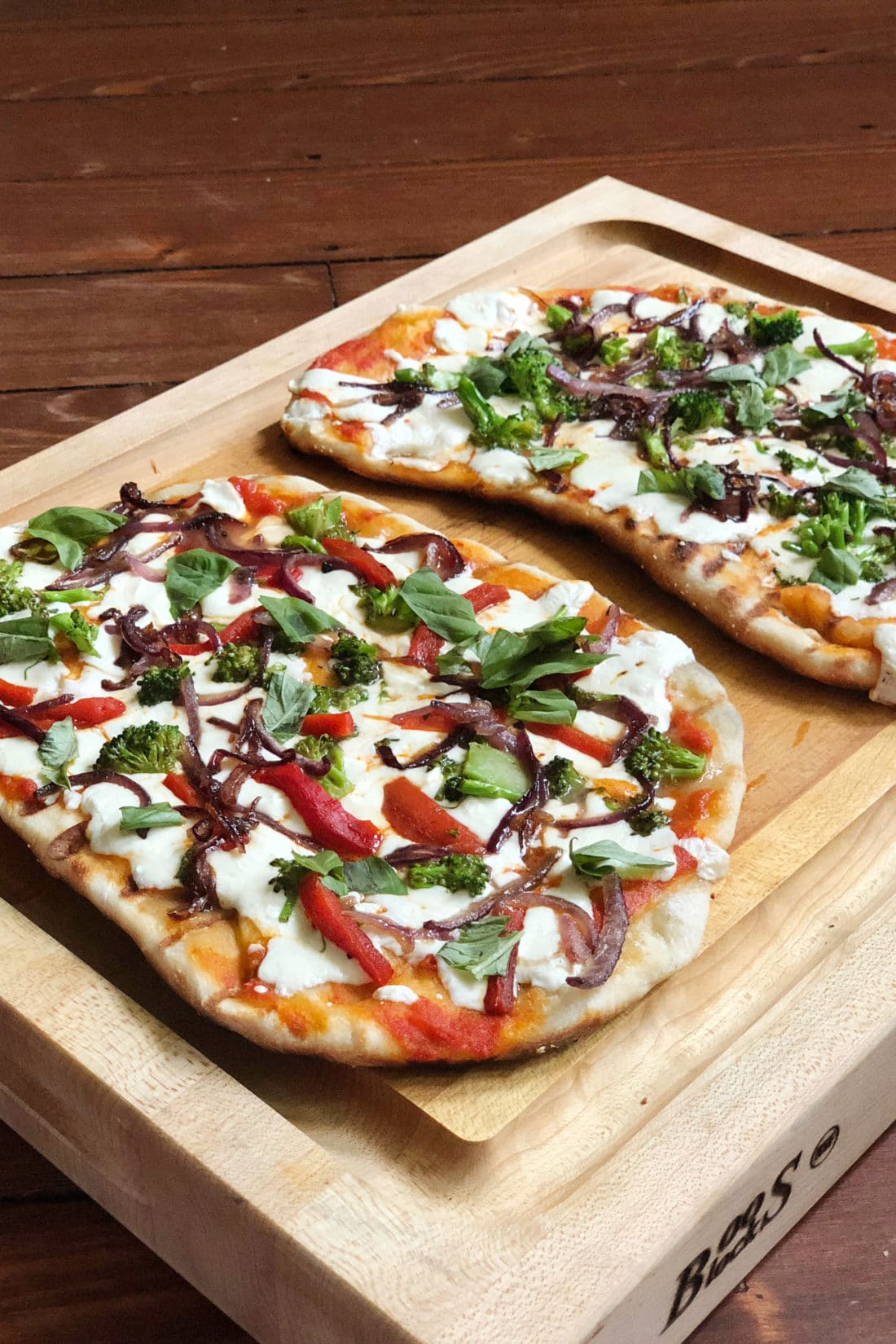 Two Grilled Pizzas on a wooden tray.