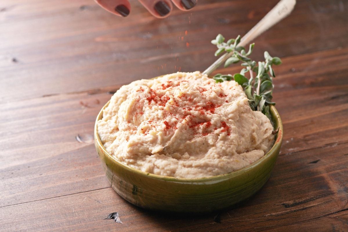Sprinkling paprika on Cannellini Bean Dip with Lemon and Parmesan in small bowl.