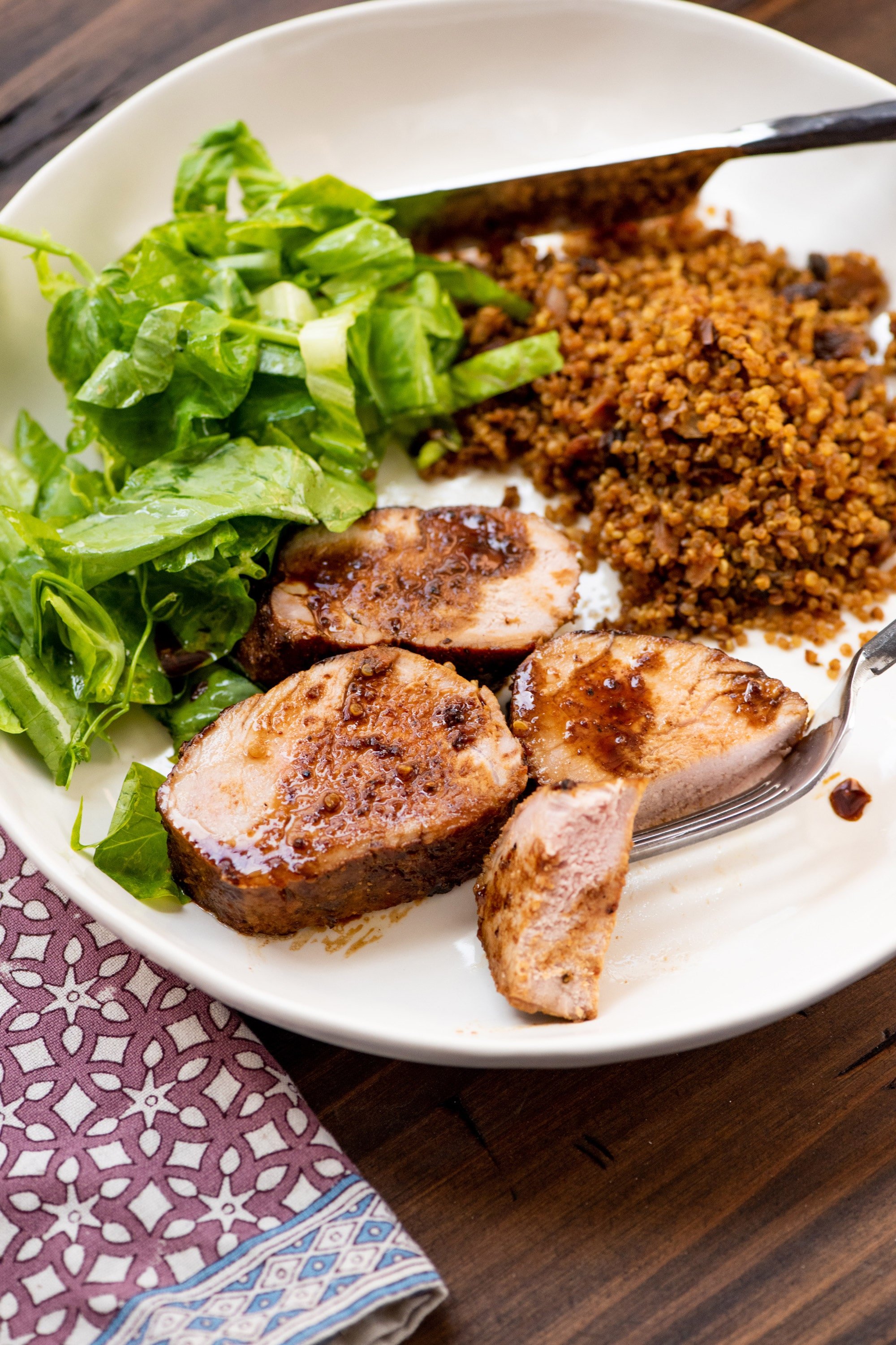 Slices of Dijon and Honey Crusted Pork Tenderloin on a plate with salad and grains.