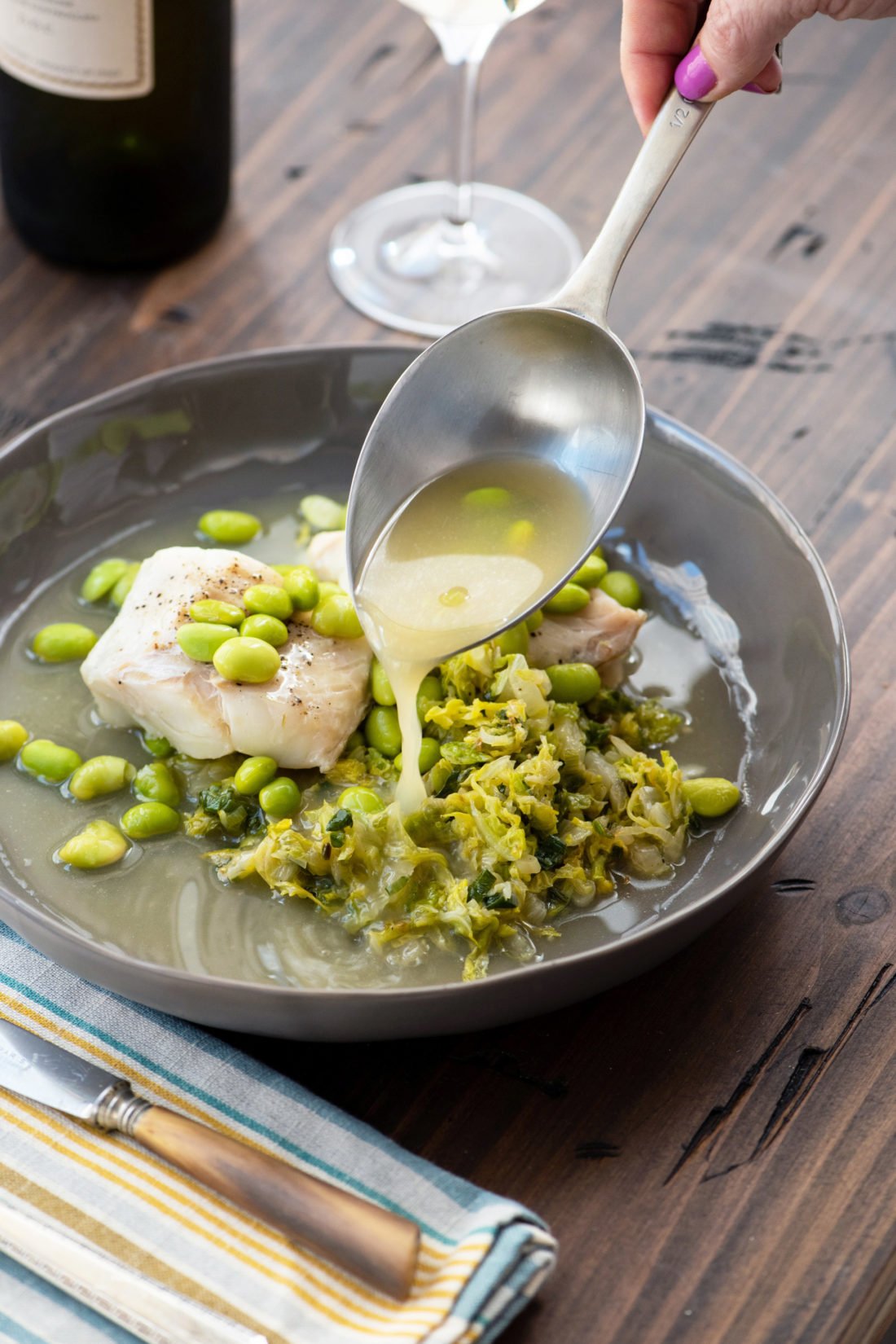 Spoon serving broth over Cod, Cabbage and Edamame.