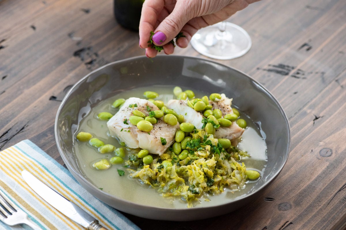 Woman sprinkling parsley onto Cod, Cabbage and Edamame.