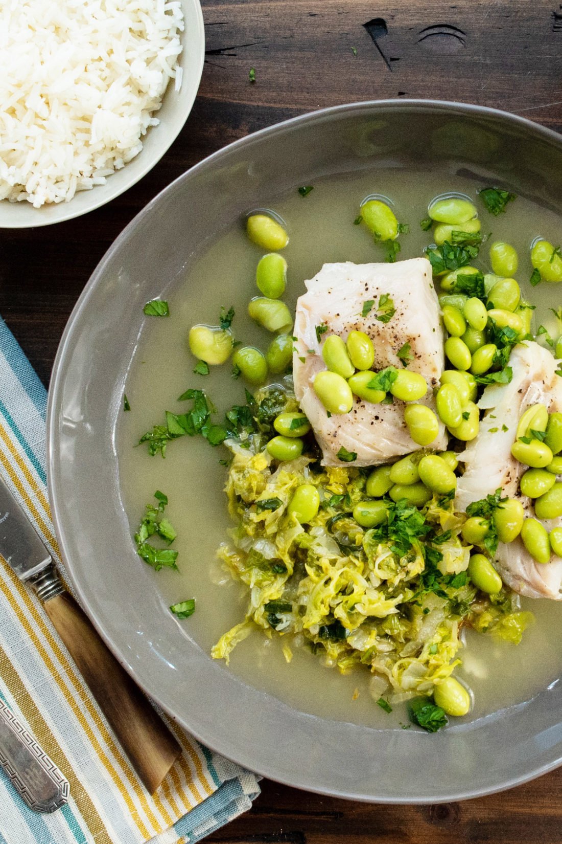 Cod, Cabbage and Edamame sitting in broth on a plate.