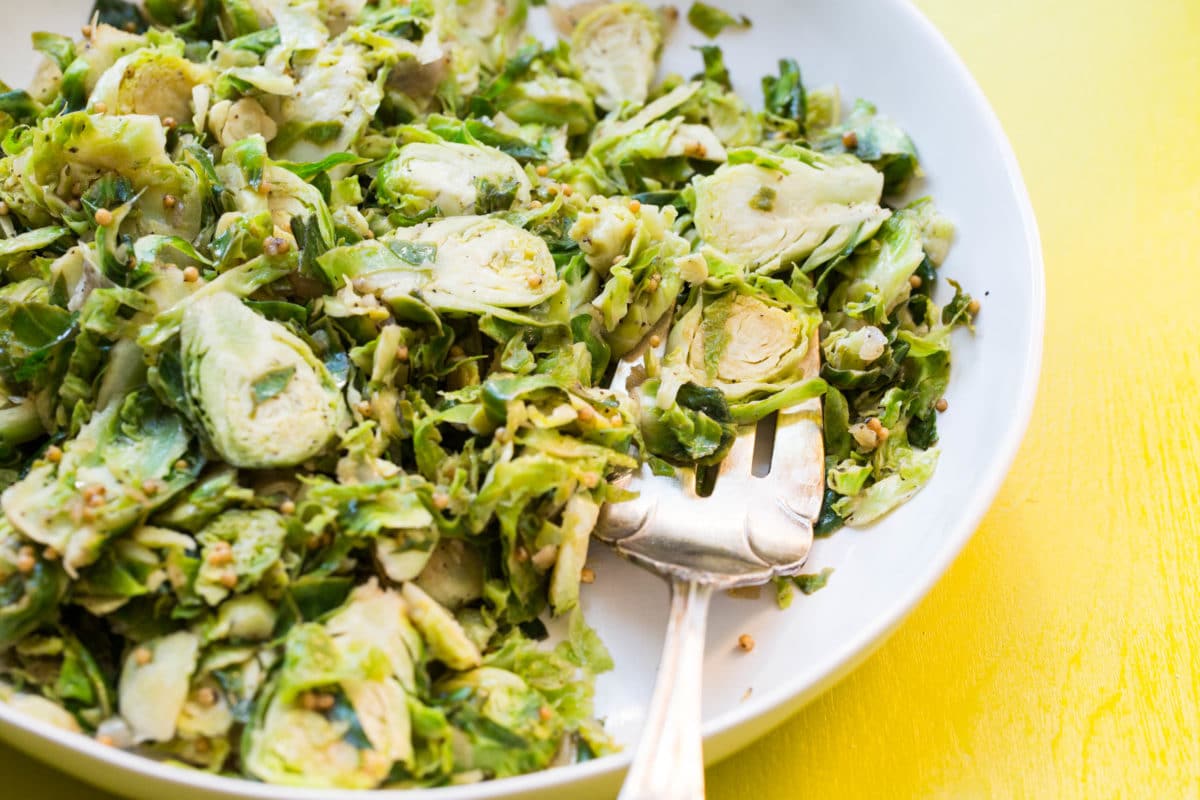 Shredded Brussel Sprouts on a white plate set on a yellow table.