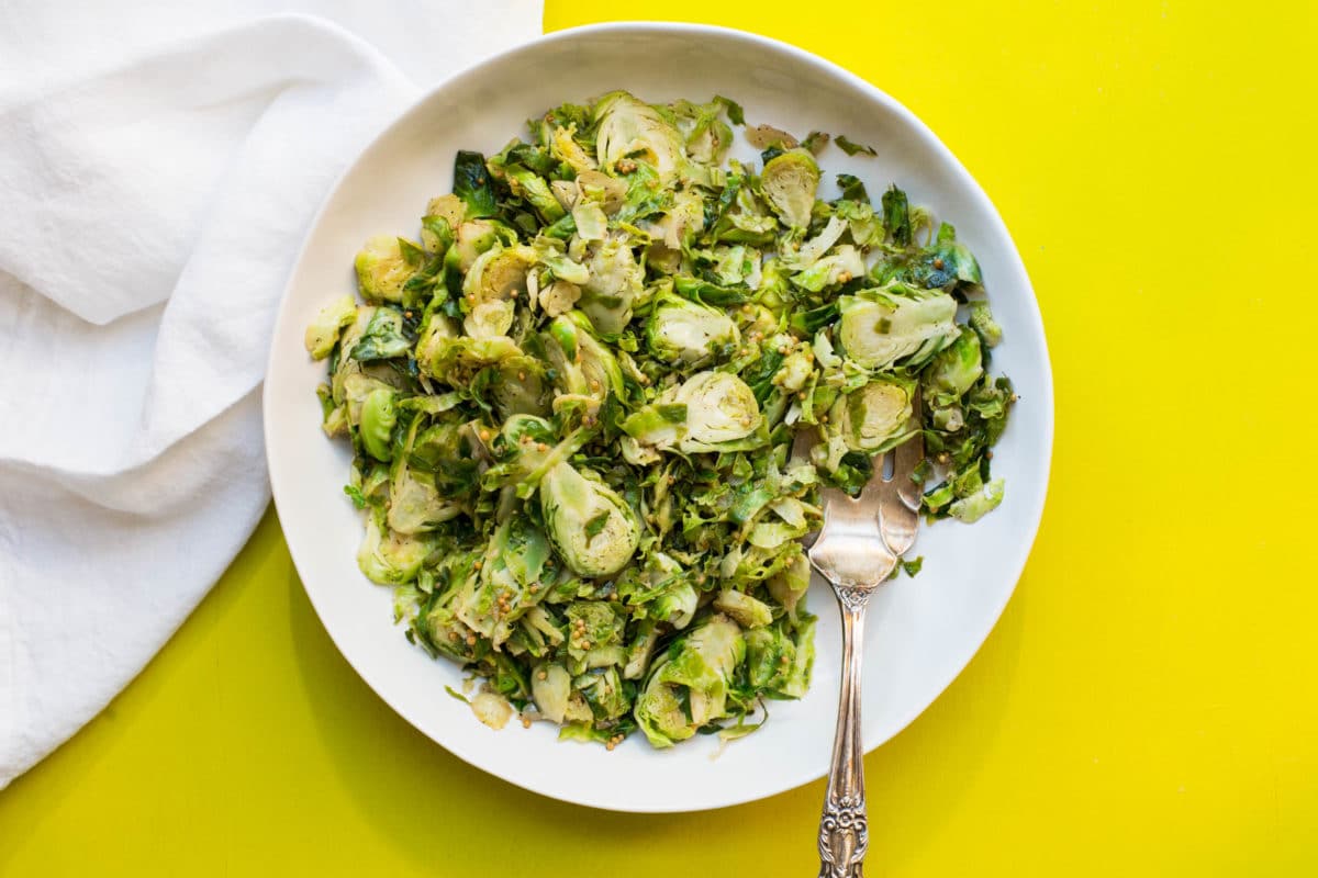 White plate of Shredded Brussel Sprouts on a yellow table.
