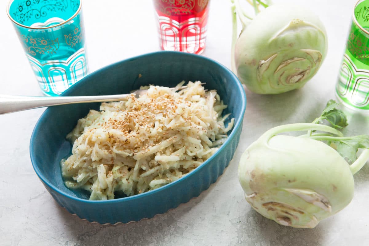 Fork in a dish of Asian Kohlrabi and Apple Slaw on a table with two kohlrabies.