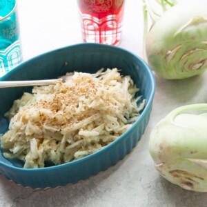 Fork in a dish of Asian Kohlrabi and Apple Slaw on a table with two kohlrabies.